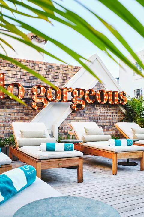 A lit-up sign that says 'gorgeous' above sun loungers