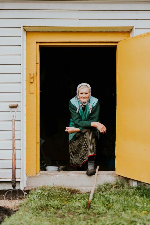 A elderly woman stares out a door