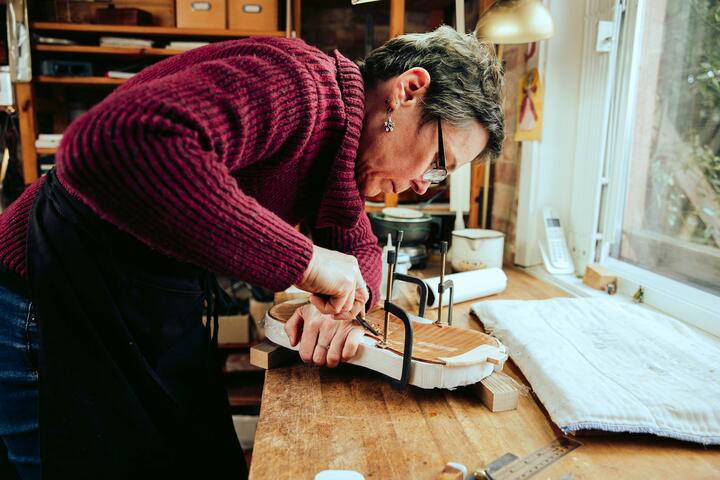 A woman chisels the wooden body of a violin