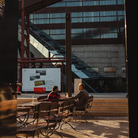 Two men have a beer in an industrial restaurant garden